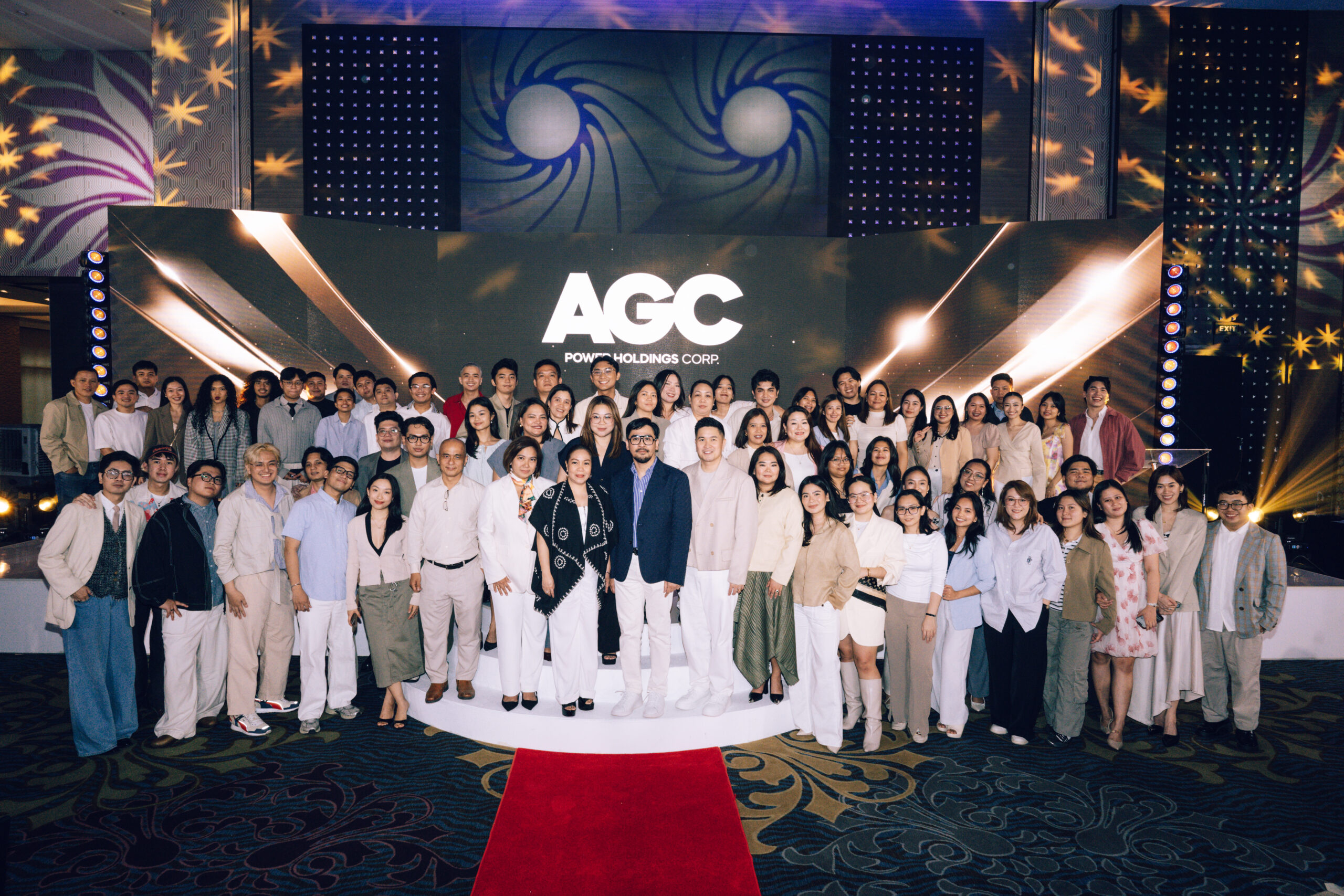 Group of people posing on stage in front of an AGC Power Holdings backdrop with a red carpet in the foreground.