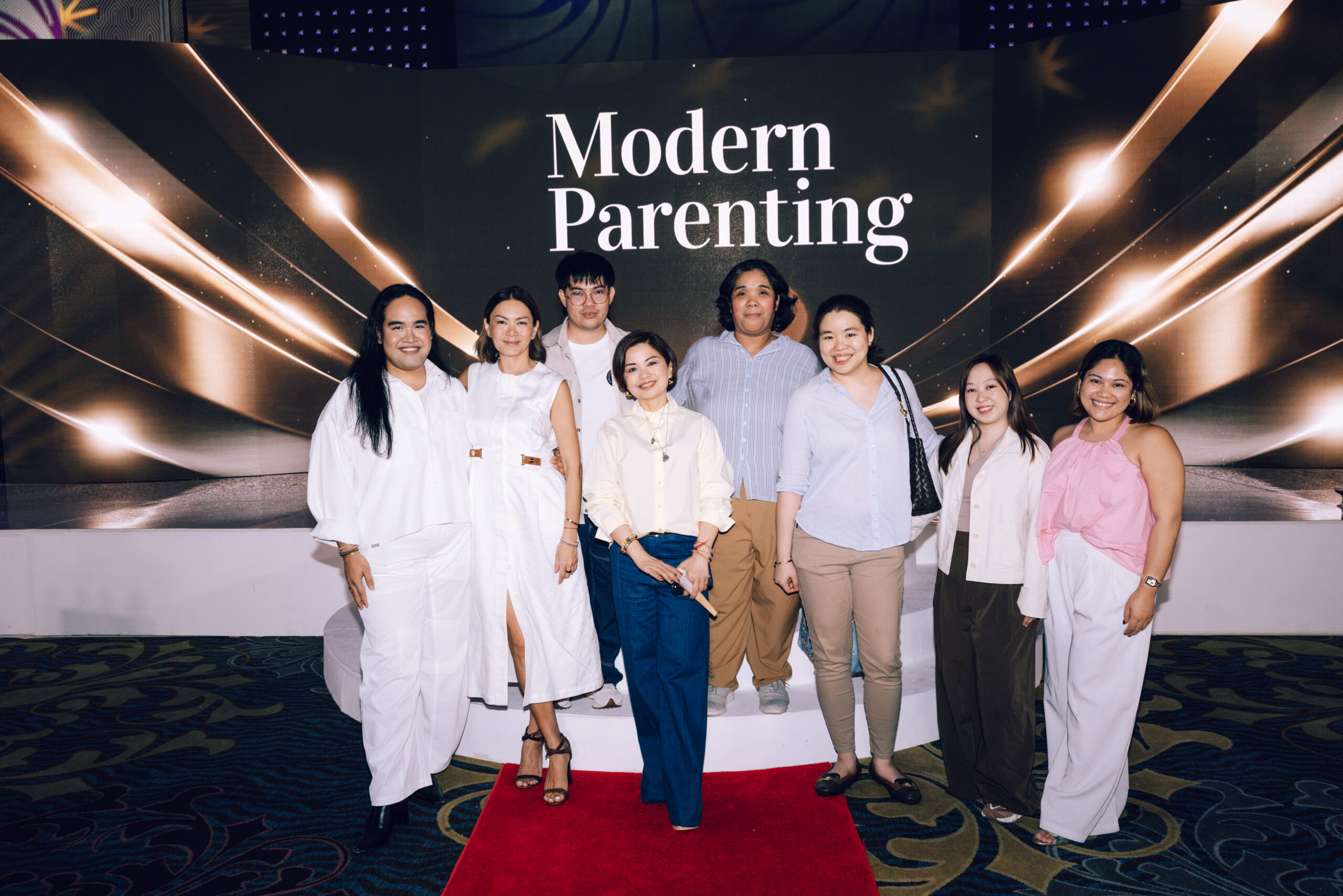 Group of eight adults posing on a red carpet in front of a 'Modern Parenting' backdrop.