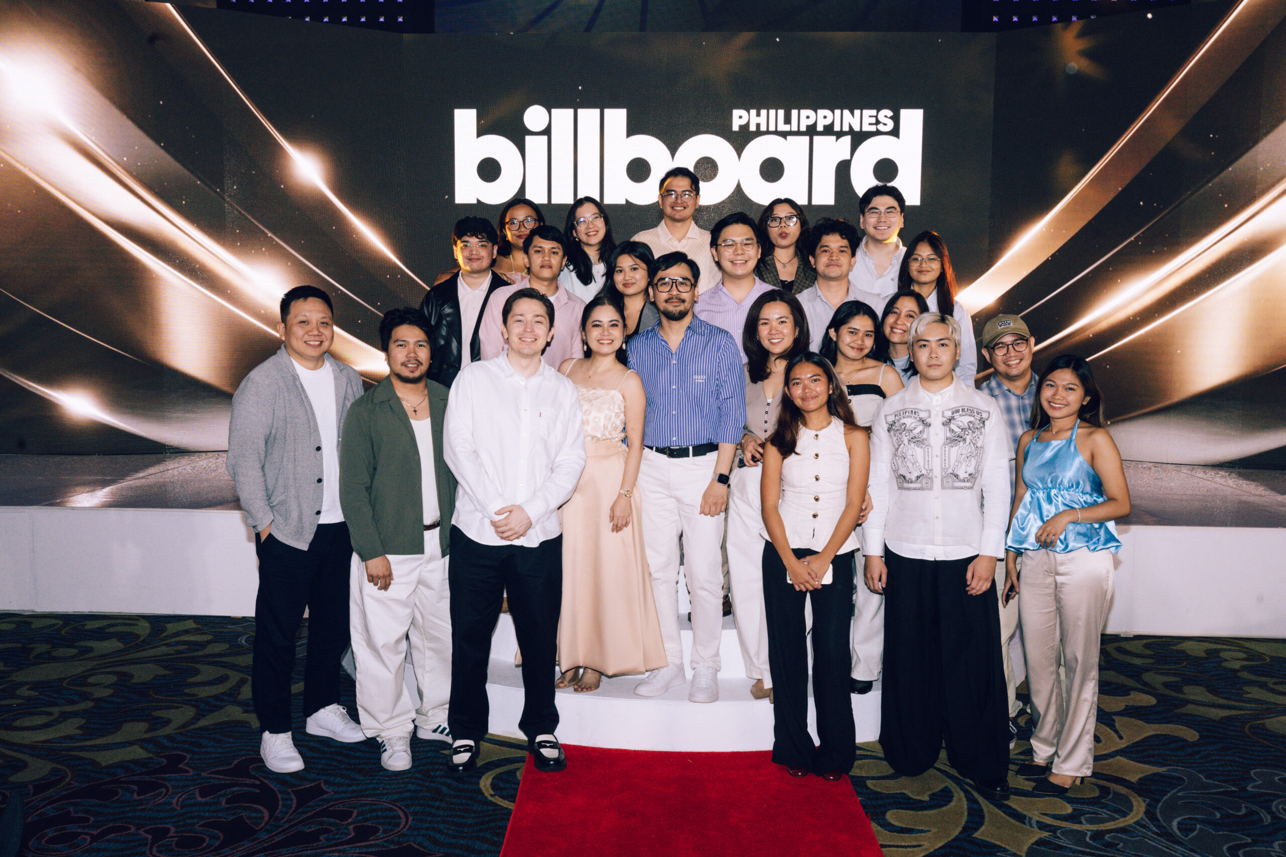 Group of people posing for a group photo on stage with a large Billboard Philippines backdrop behind them and a red carpet beneath.