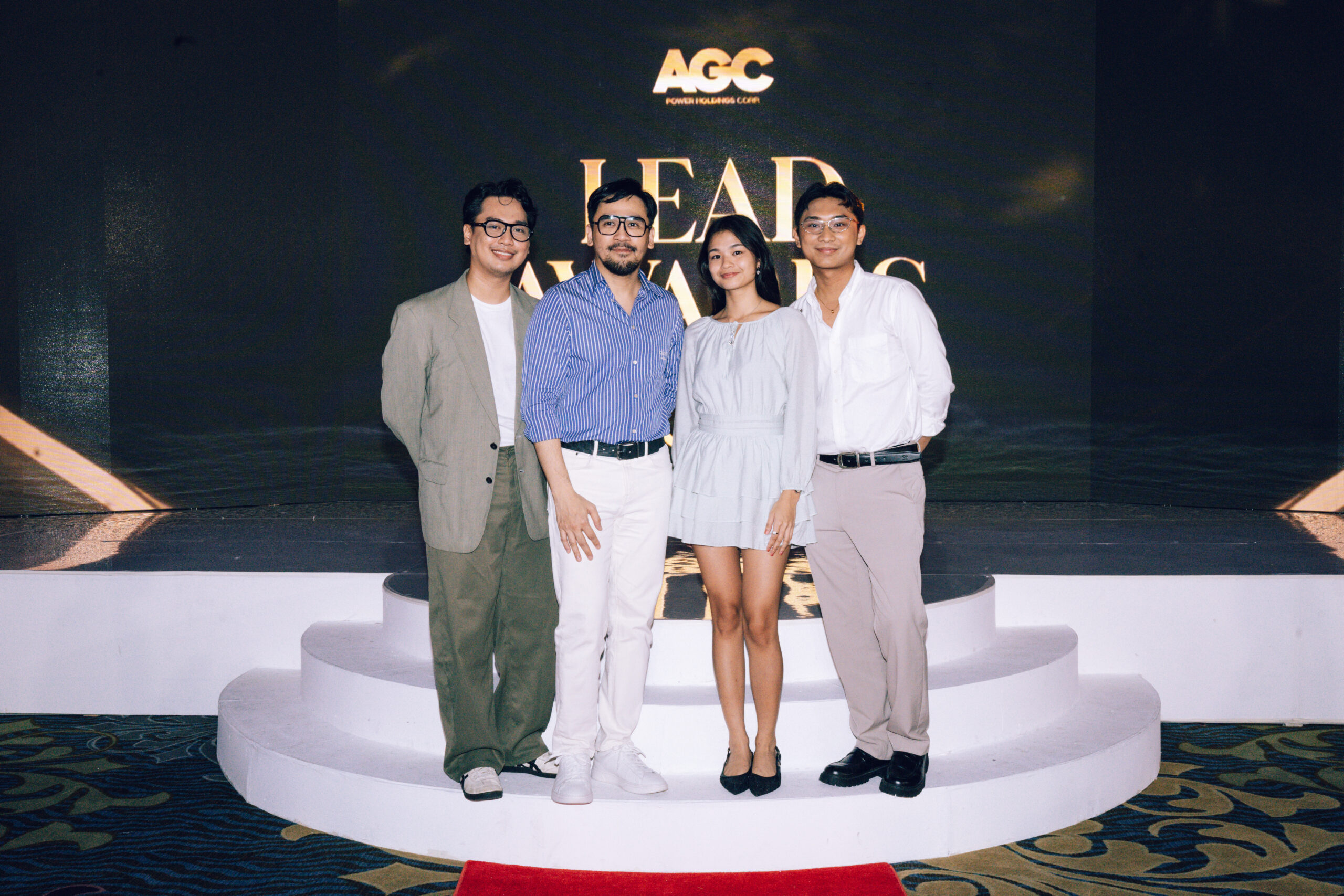 Four people stand together on a white circular stage with a dark backdrop and large 'LEAD' sign behind them.
