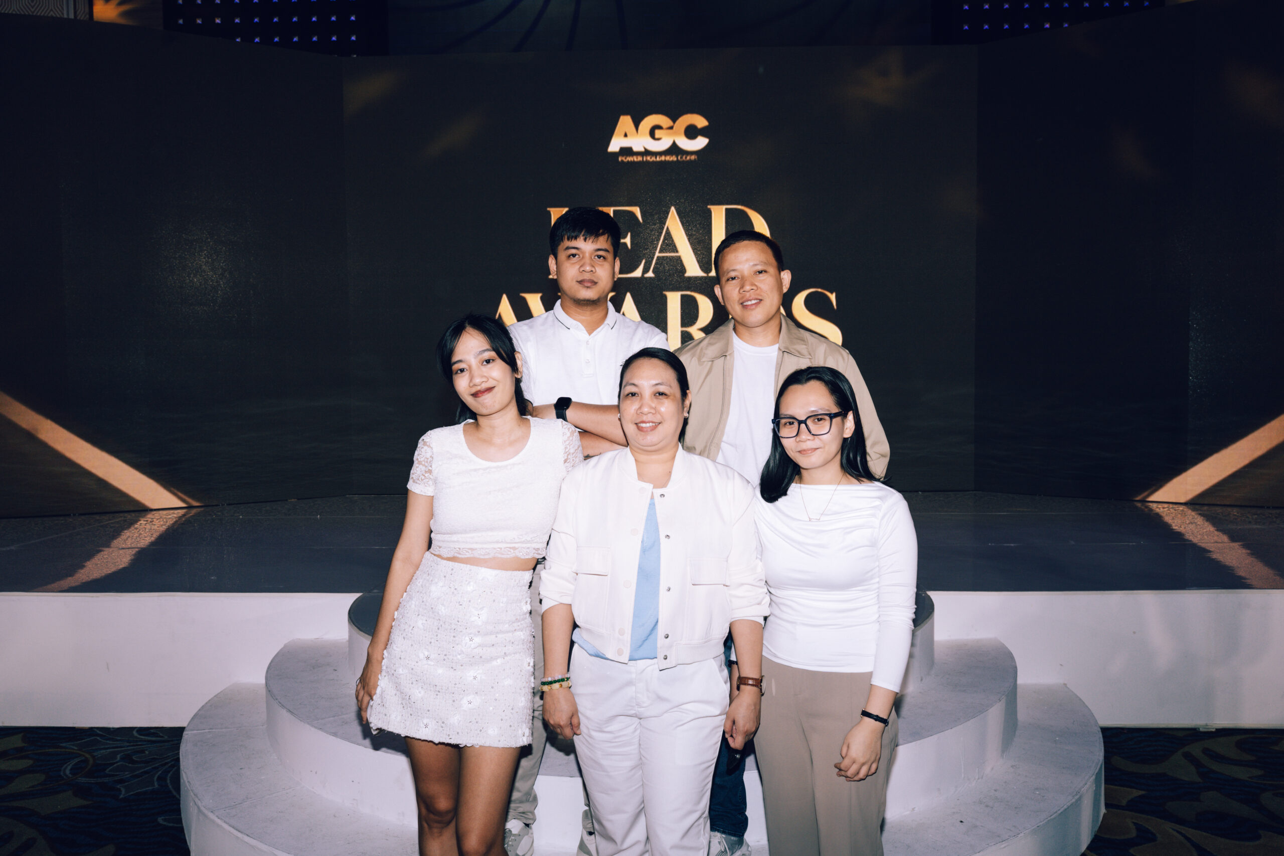 Group of five people posing on white circular platforms at an awards event backdrop that reads 'LEAD AWARDS' and displays the AGC logo in gold.