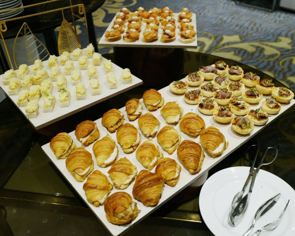 Assorted pastries and finger foods arranged on white platters at a buffet table.