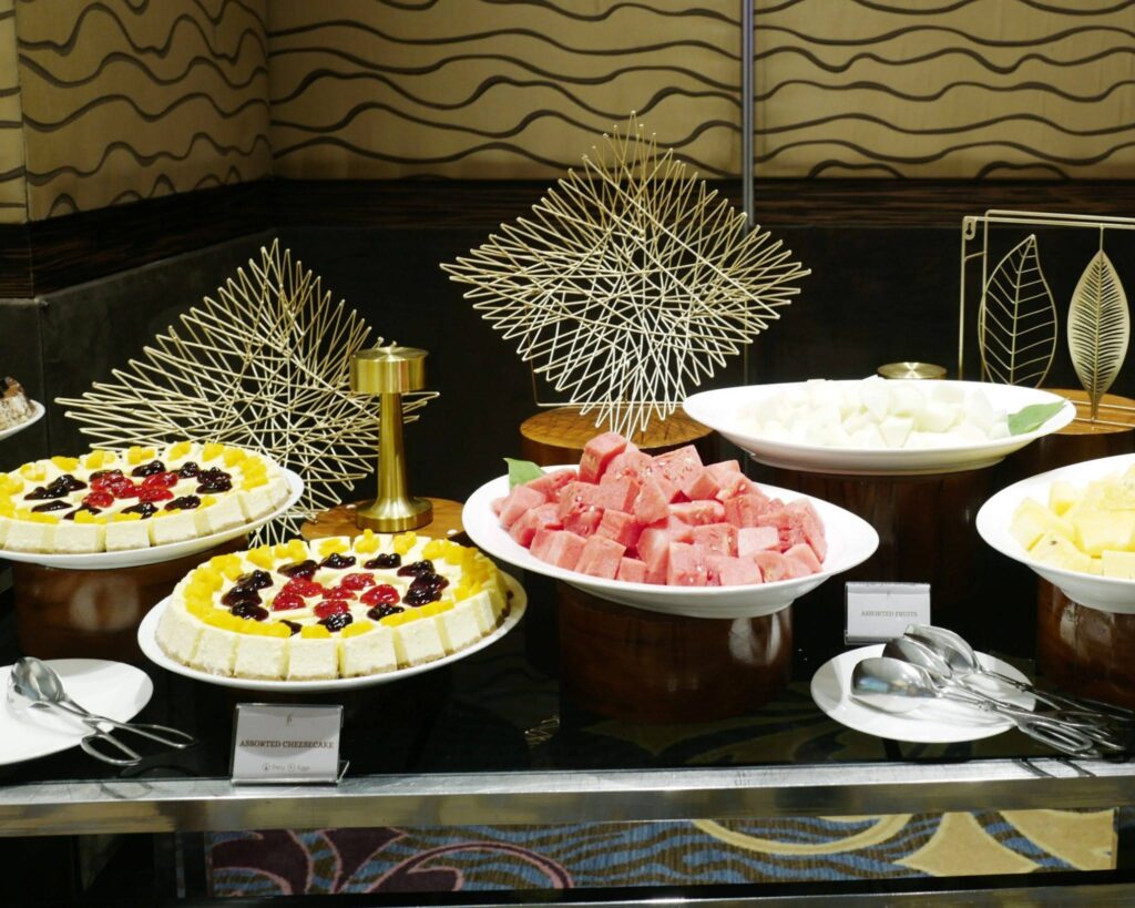Assorted fruit-topped cheesecakes on display with decorative spiky sculptures in a buffet setting.