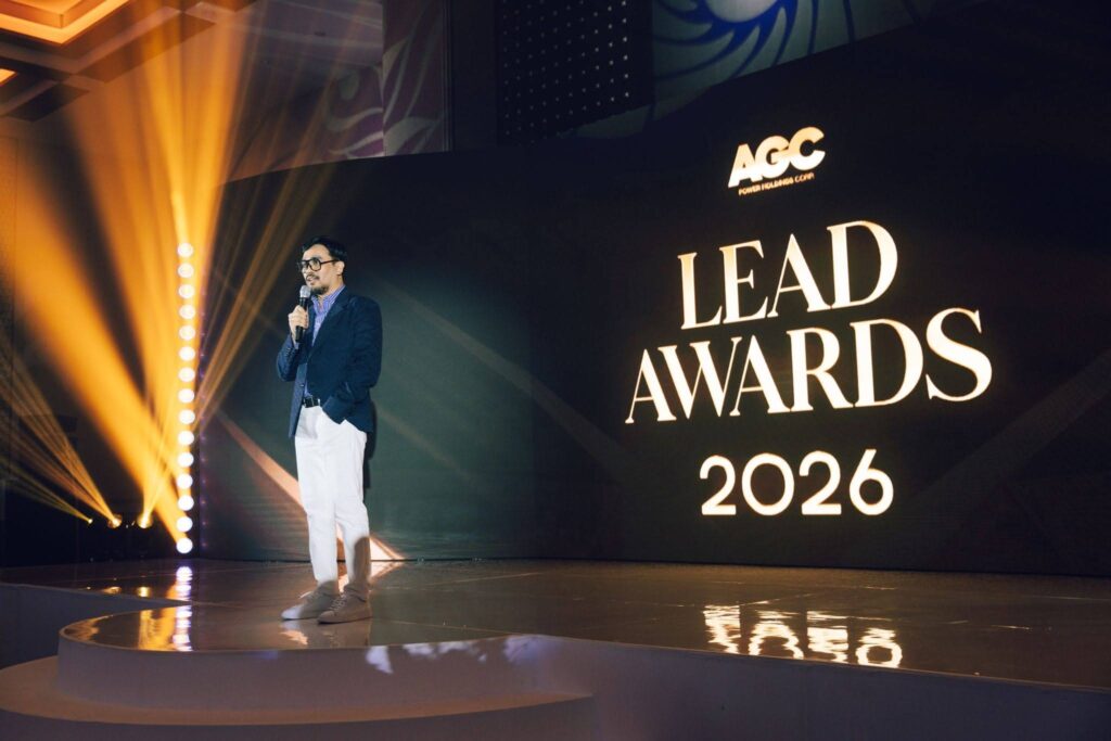 Male host in a blue blazer speaks into a microphone on stage at the Lead Awards 2026, AGC logo visible.