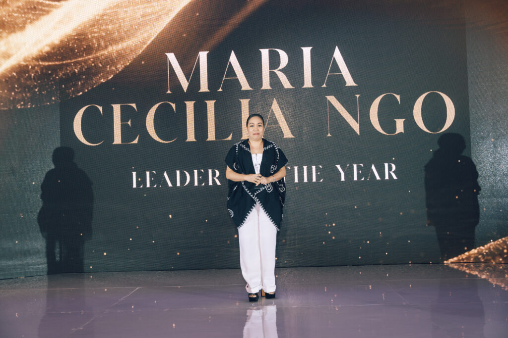 Woman posing on stage in front of a large display that reads 'MARA CECILIA NGO' and 'LEADER OF THE YEAR'
