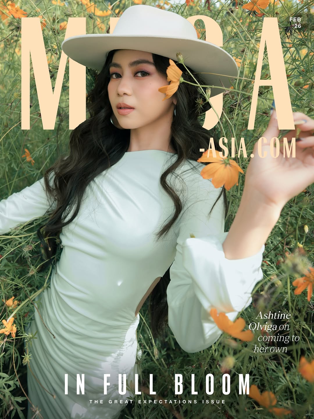 Magazine cover portrait of a woman in a pale mint dress and white hat, standing amid orange flowers; cover line 'In Full Bloom'.