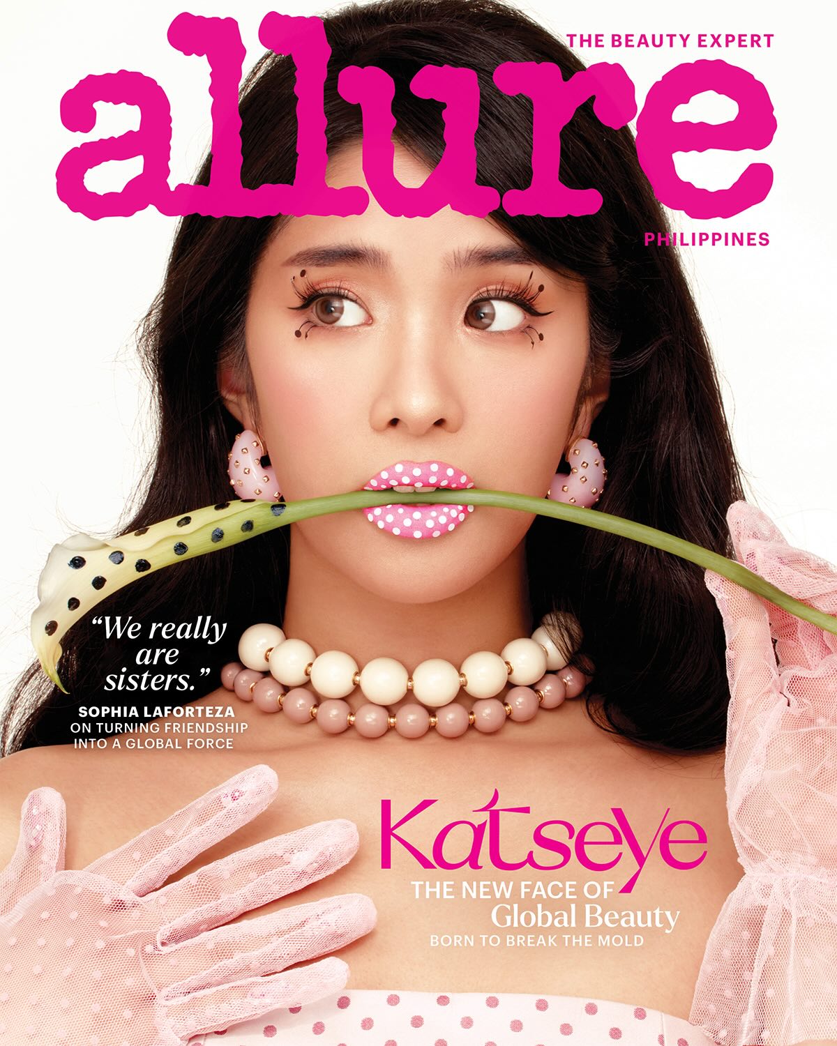Close-up of a woman biting a green stem with pink polka-dot lips, wearing pink gloves and pearl necklace on a glossy beauty magazine cover.