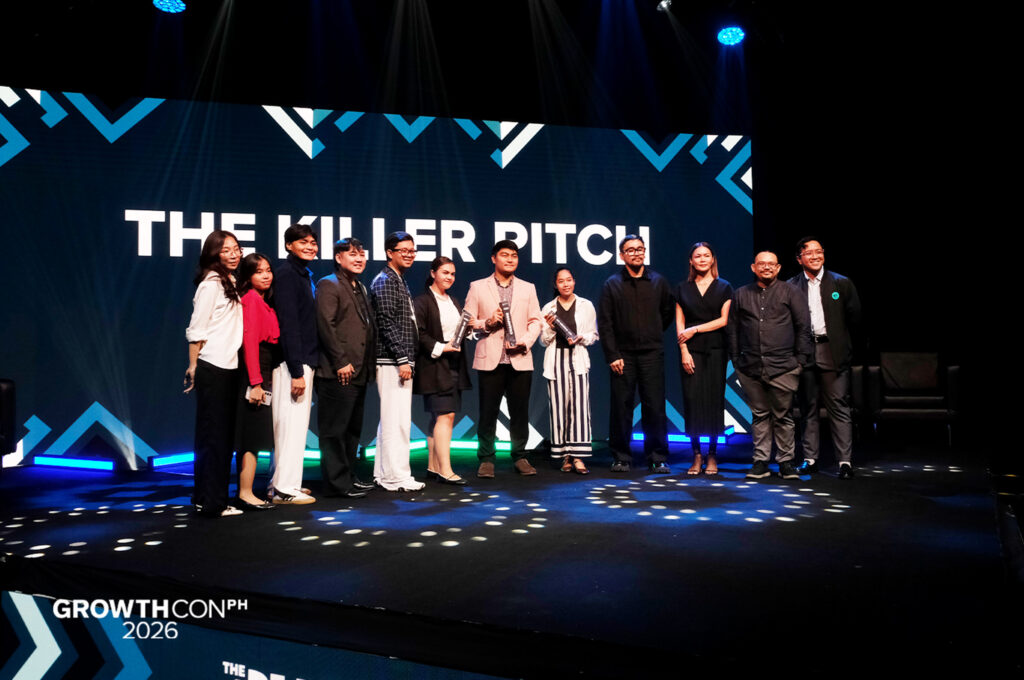 Group of people on a stage posing with awards at a conference, backlit by a large screen reading 'THE KILLER PITCH' and 'GrowthCon 2026' banner.